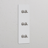 Panneau triple Peignable Nickel Poli avec six Interrupteur VV à Levier x6 Interrupteurs verticaux sur un mur texturé blanc.