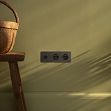 Plaque triple avec prise USB-C 30W et double prises Type E en bronze et noir sur mur vert.