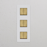 Panneau triple interrupteur vertical en Laiton Ancien, composé de six interrupteurs carrés en bronze avec inserts blancs.
