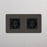 Prese Modulo Doppio 2x Schuko/Bipasso color bronzo-nero su parete bianca testurizzata, per la compatibilità con due spine.