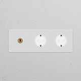 Triplo interruttore a levetta con 2x modulo Schuko tipo F, finitura pitturabile ottone antico bianco su parete bianca.