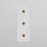 Interruptor articulado vertical de três vias triplo em Latão Antigo Pintável, em painel retangular branco.