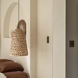 Bronze single 2x Toggle Switch wall-mounted on the right side of the wall with the Bronze Double vertical switch on the left wall with wooden wickered lampshade hangin in front from ceiling. 