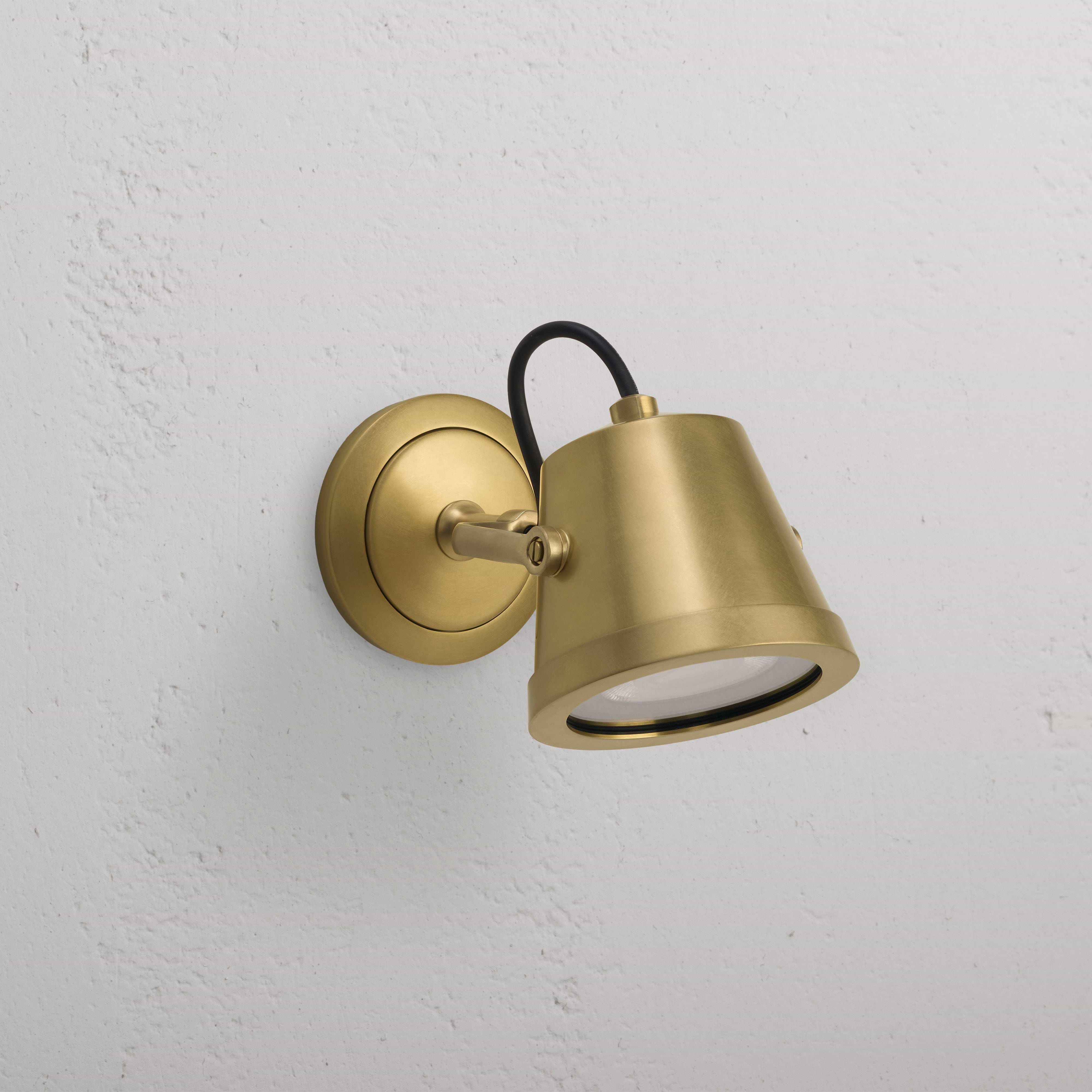 Cambridge Wall Floodlight in antique brass, cone-shaped outdoor floodlight mounted on a textured white wall.
