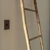 Bronze Single Toggle Switch wall mounted onto a cream wall on the left with a bamboo ladder to the right. 