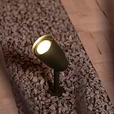 Bronze Ealing Ground Spotlight illuminating light upwards from a stone gravel flooring below. 