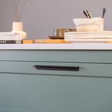 Oxford Edge Pull Handle 128mm Bronze Finish on White Backgroundaffixed to a dark green kitchen draw with a marble top and ornaments  