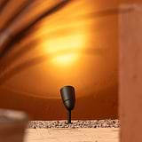 Bronze Ealing Ground Spotlight projecting upwards light onto a stone wall from stone grave flooringl below. 