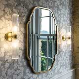 Claremont Medium Wall Light Fluted Glass Antique Brass Finish White Background affixed to a floral wallpapered wall next to an antique brass framed mirror