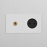 Round paintable antique brass black double toggle switch and Schuko Type F power module on a white wall.