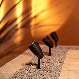 Bronze Ealing Ground Spotlights projecting upwards light onto a stone wall from stone gravel flooring below. 