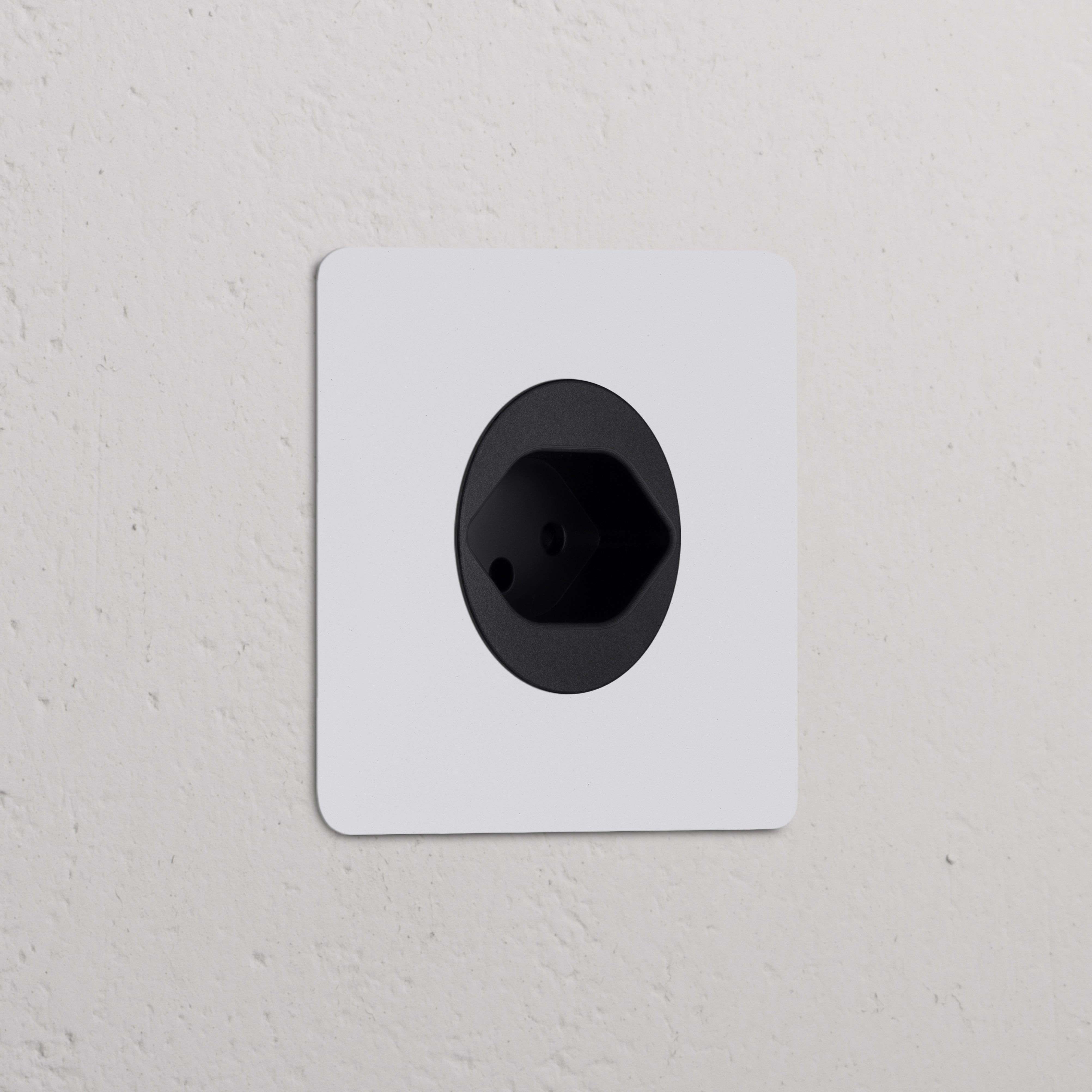 Paintable black Single Swiss Type J power module socket, round design, wall-mounted on a textured surface.