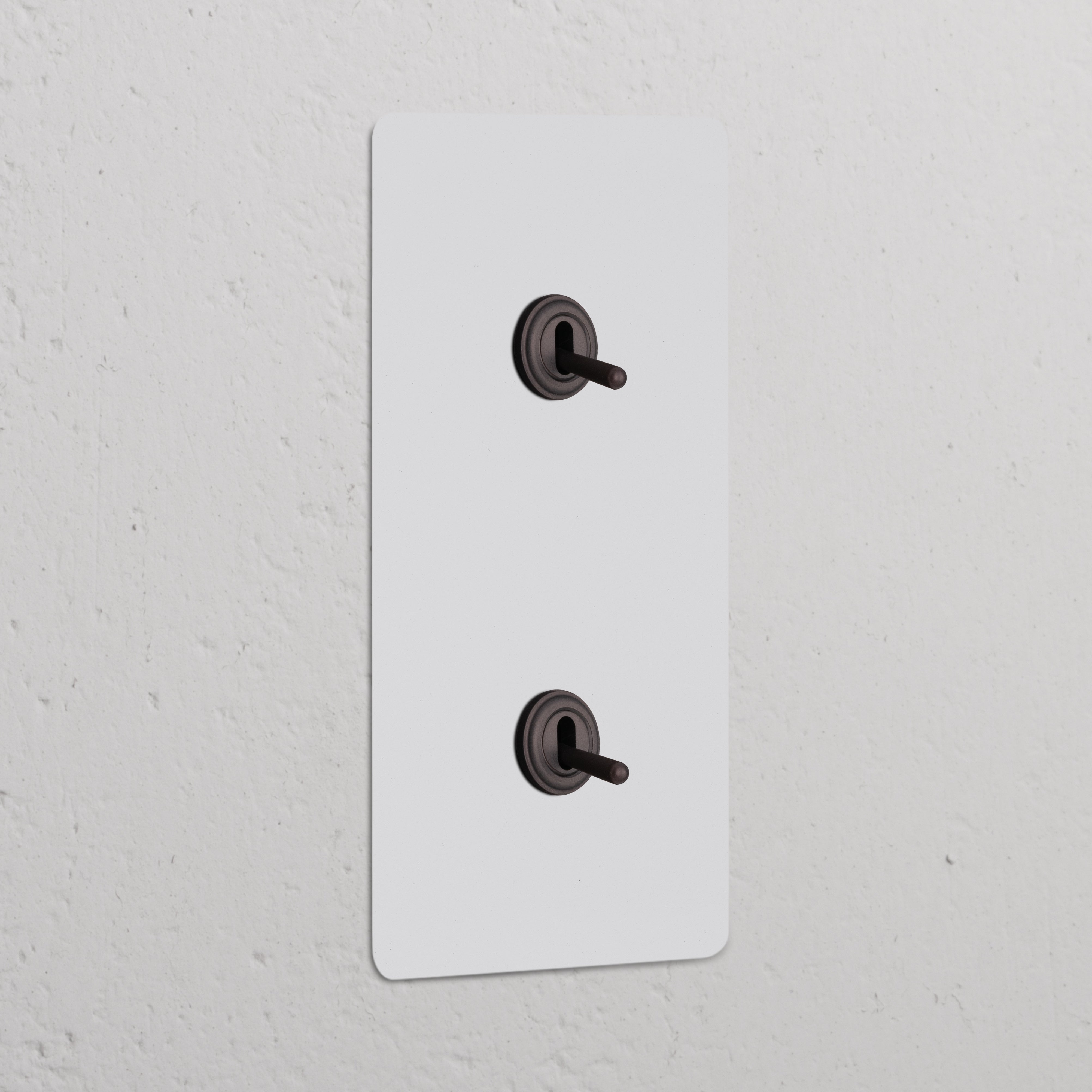 Double 2x Vertical Toggle Switch in paintable bronze, featuring two black toggles, mounted on a wall.