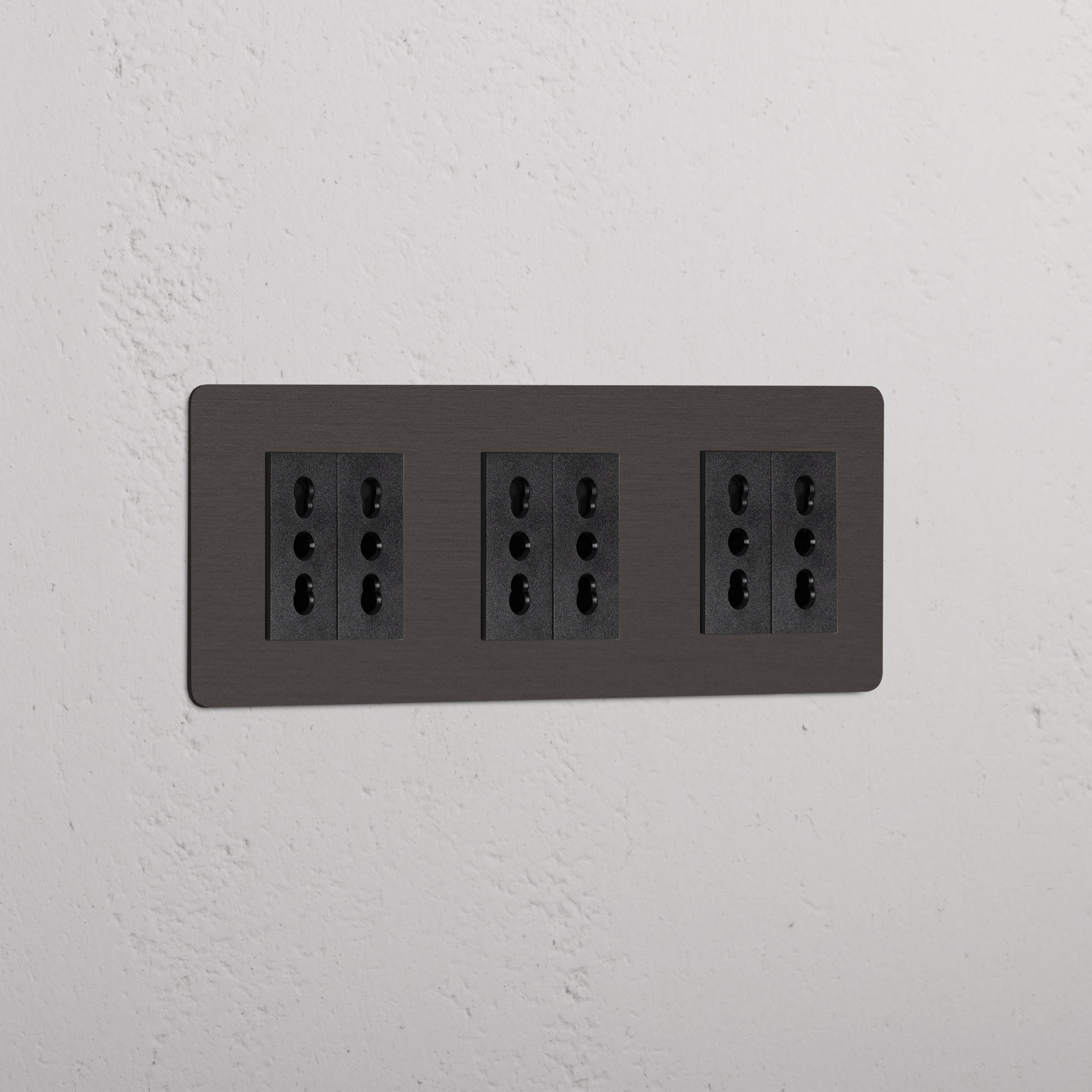 Triple 6x Bipasso Module in Bronze Black, a sleek triple socket panel on a white textured wall.