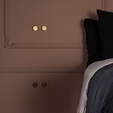 Double 2x French/Belgian Type E power module round in paintable black on a wall near a bed.
