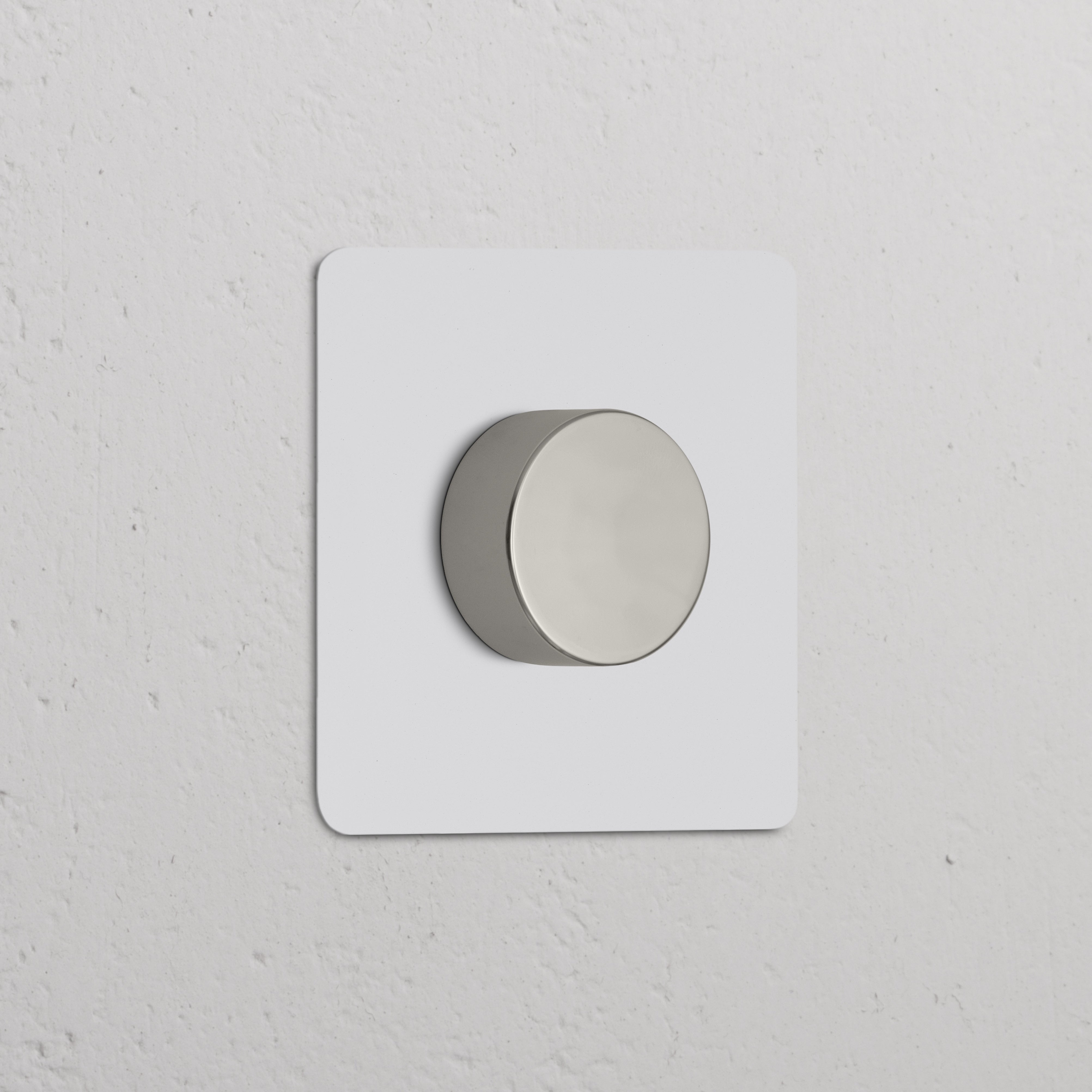 Paintable polished nickel single dimmer switch on a minimalist white wall.