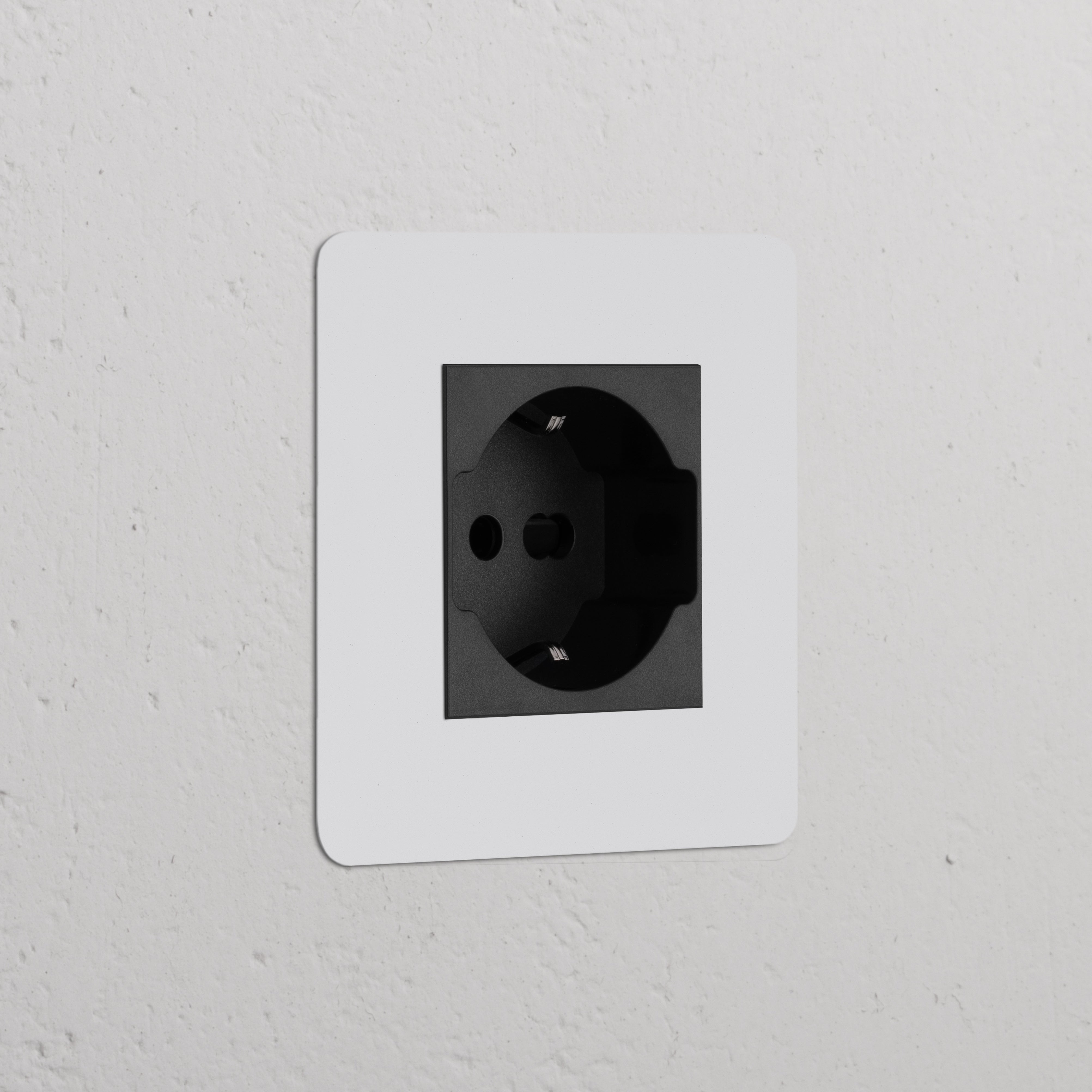 Single Schuko/Bipasso power module in paintable black, set in a white frame on a textured white wall.