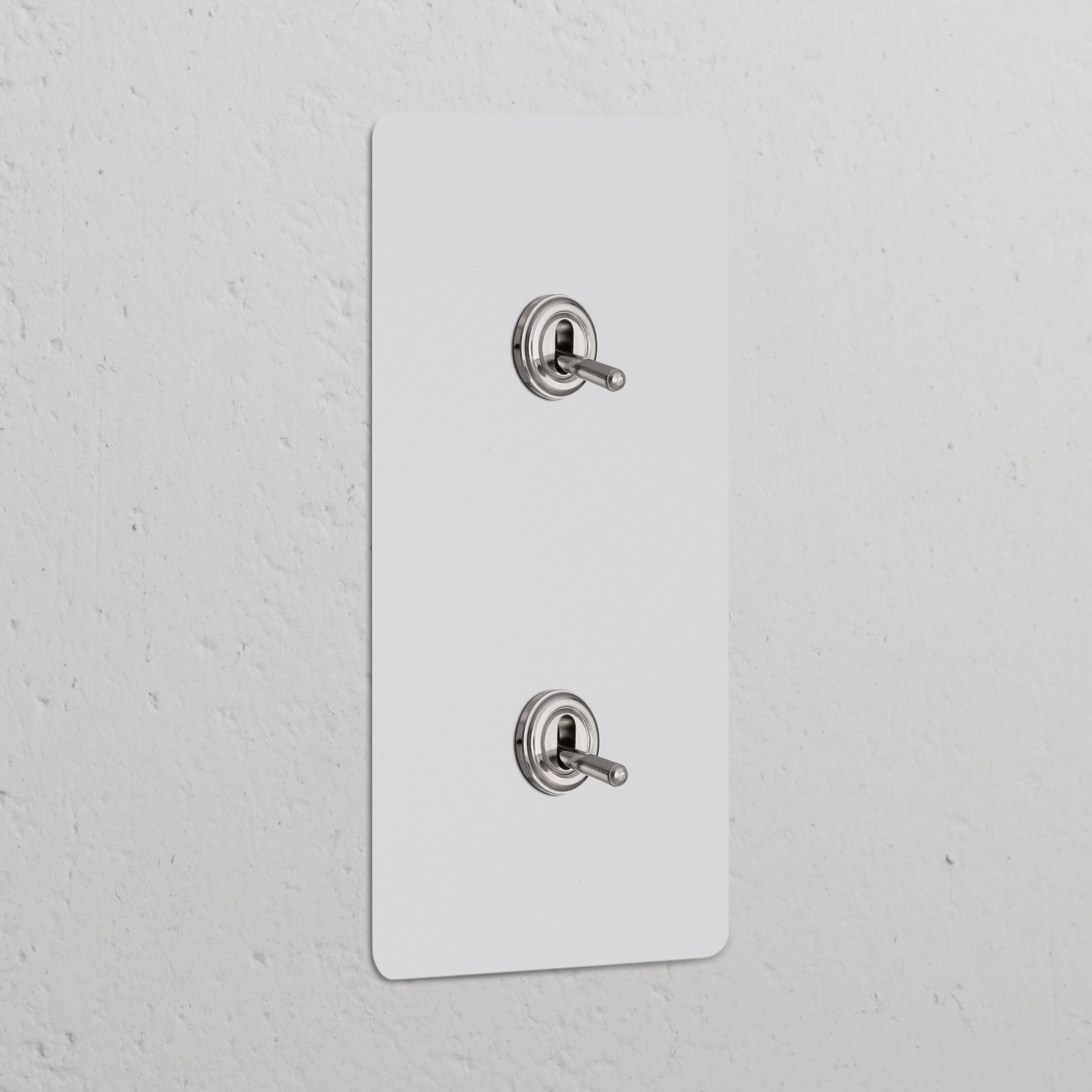 Double 2x vertical toggle switch in paintable polished nickel, for stylish control of lights on white wall.