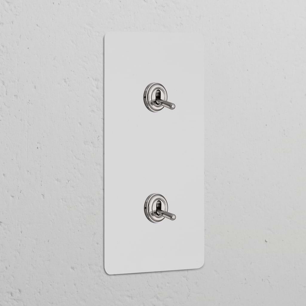 Double 2x vertical toggle switch in paintable polished nickel, for stylish control of lights on white wall.