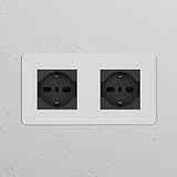 Double 2x Schuko/Bipasso power module in paintable black, featured as double sockets on a white wall.