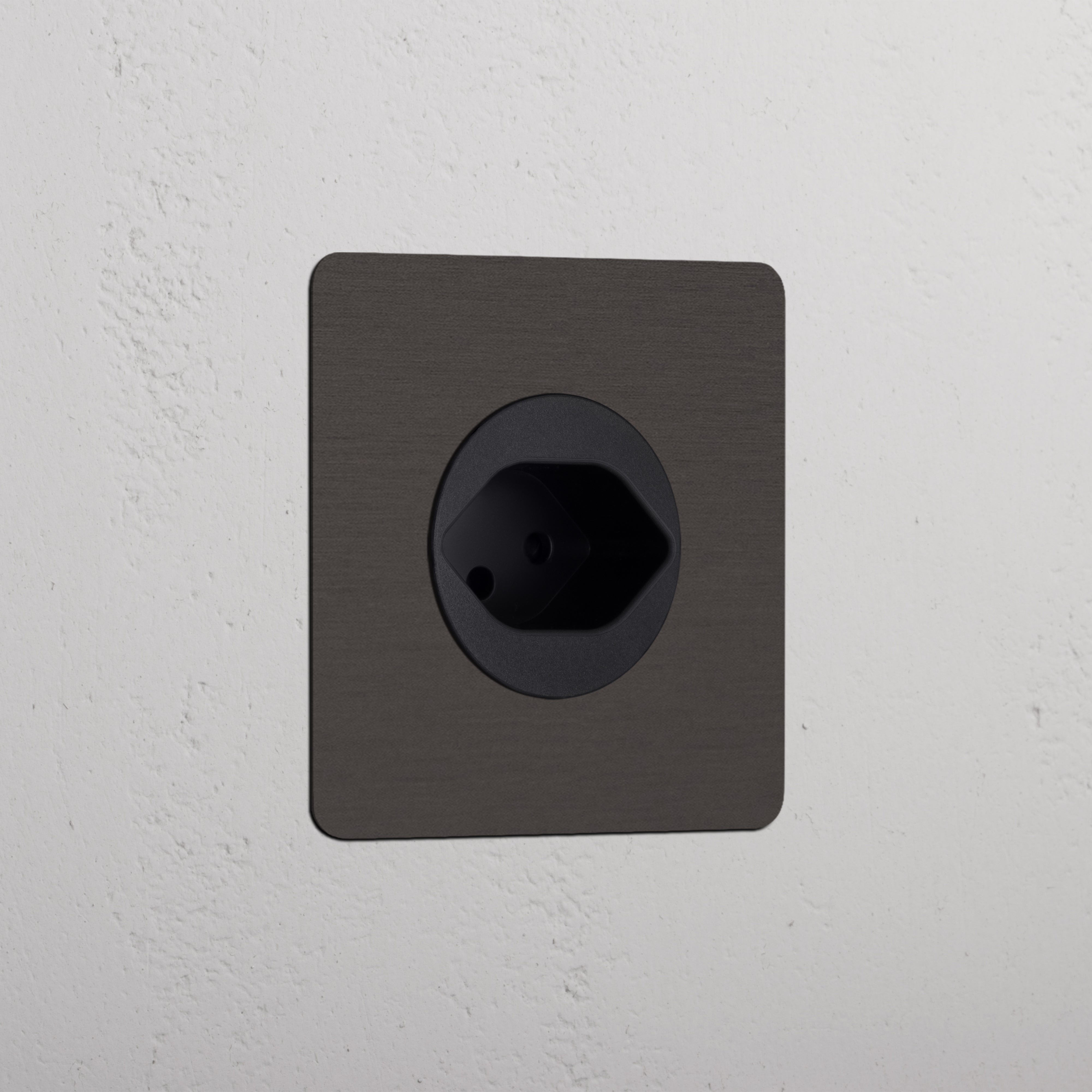 Single Swiss Module Round - Bronze Black wall socket integrated into a textured white wall.