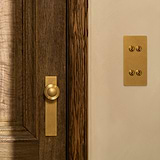 Antique Brass Poplar Long Plate Sprung Door Knob fitted to a dark wooden door, with an antique Brass 4g Toggle switch. 