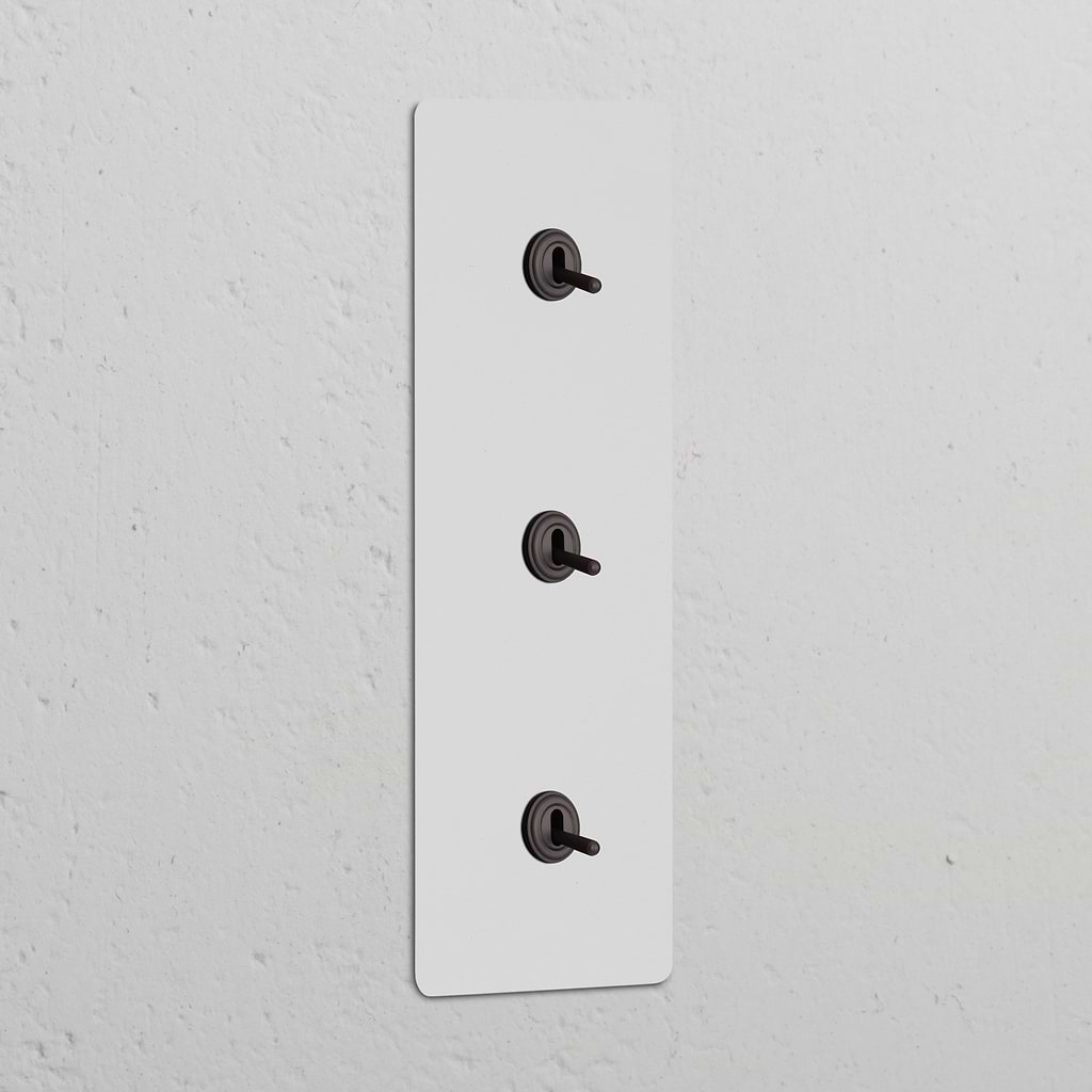 Triple 3x Vertical Toggle Switch in paintable bronze on a textured white wall.