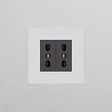 Single 2x Bipasso Power Module in paintable black, featuring two sockets on a white textured wall.