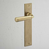 Digby Long Plate Sprung Door Handle Antique Brass Finish on White Background at an Angle