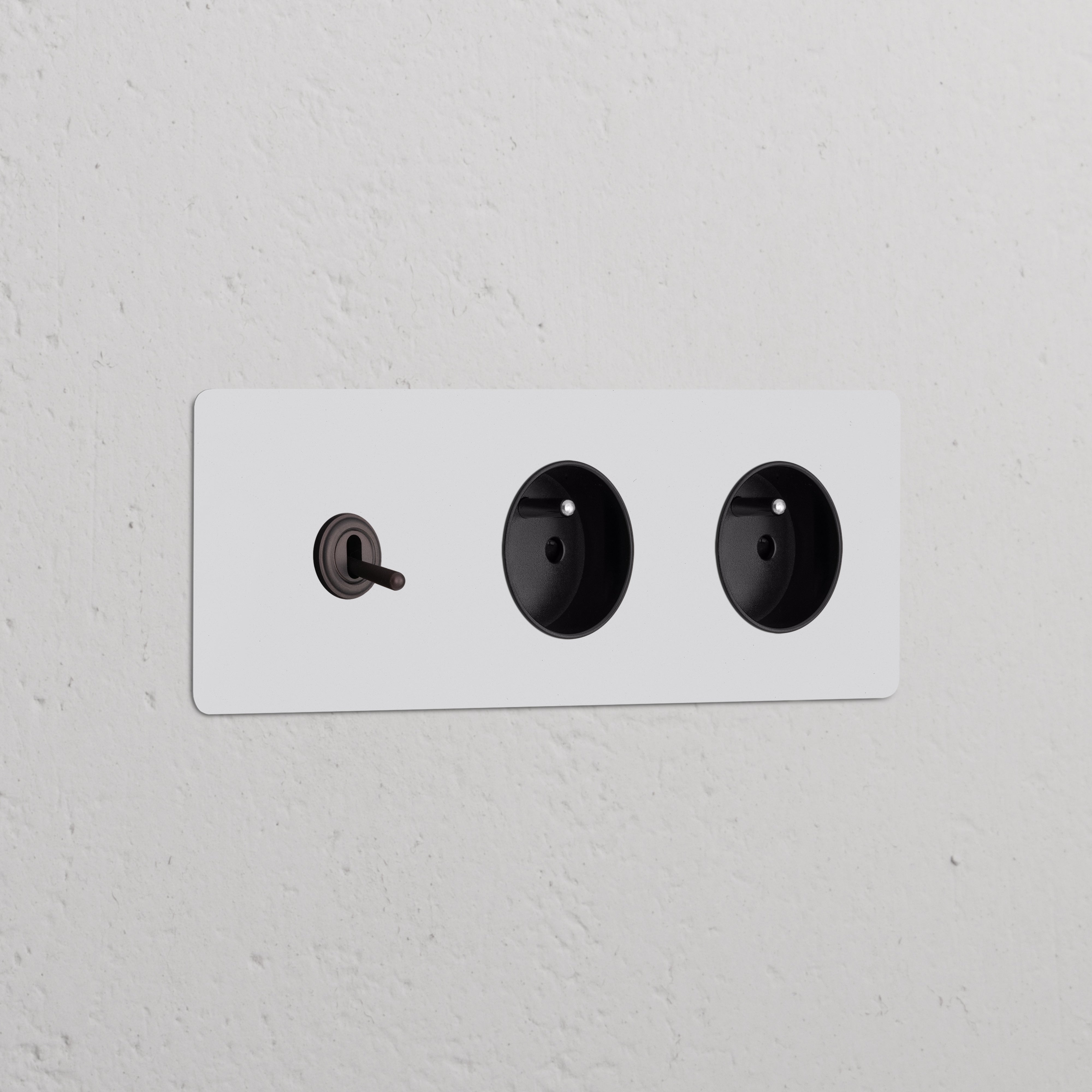 Paintable bronze black triple toggle switch with two round Type E power modules on a white wall.