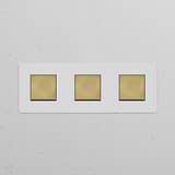 Triple 3x Rocker Switch with three brass buttons on a paintable white antique brass panel against a white wall.