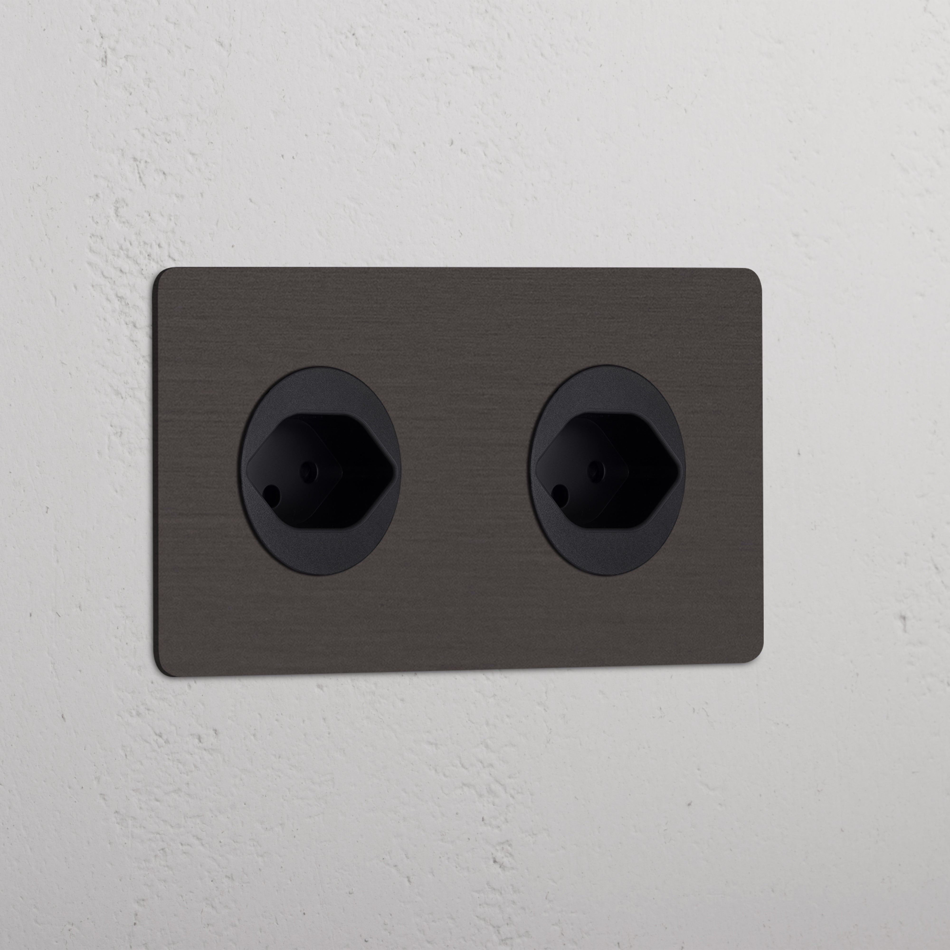 Bronze Black Double 2x Swiss Module Round, dual sockets for electrical connections on a white textured wall.