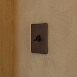 Bronze Single Toggle Switch mounted to a textured cream wall, looking from the right side. 
