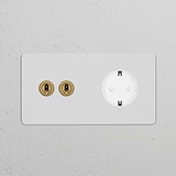 Double 2x Toggle Switch + Schuko Type F Power Module in Antique Brass and White, paintable, on a textured gray wall.