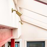 Antique Brass Bayliss Single 50mm Spotlight fitted  to a white wall on the left with red metal beam beneath. 