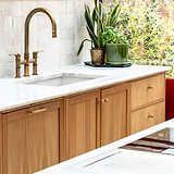 Antique Brass Bayswater Furniture Knob fitted to a cupboard door and drawers located beneath a white marble top sink with matching antique brass tap with tiled wall and plants ontop of surface.