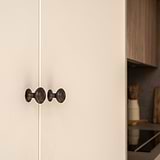 Bronze Barlow Furniture Knob on beige cabinet doors, showing dark round handles in a cozy kitchen setting.