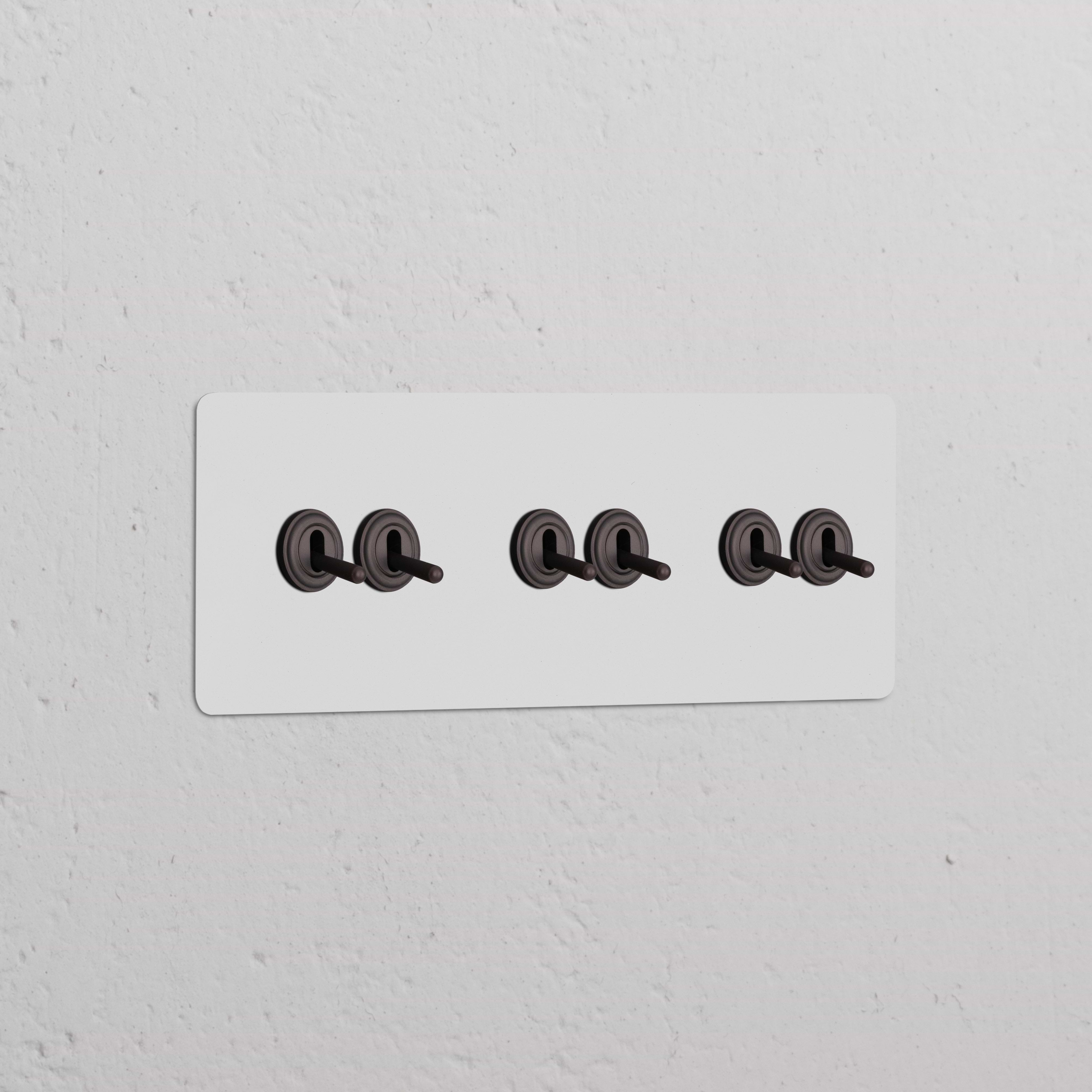 Wall-mounted Triple 6x Toggle Switch in Paintable Bronze with black toggles on a white background.