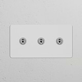 Paintable polished nickel double 3x toggle switch, sleek design for Double Switches & Dimmers on a white wall panel.
