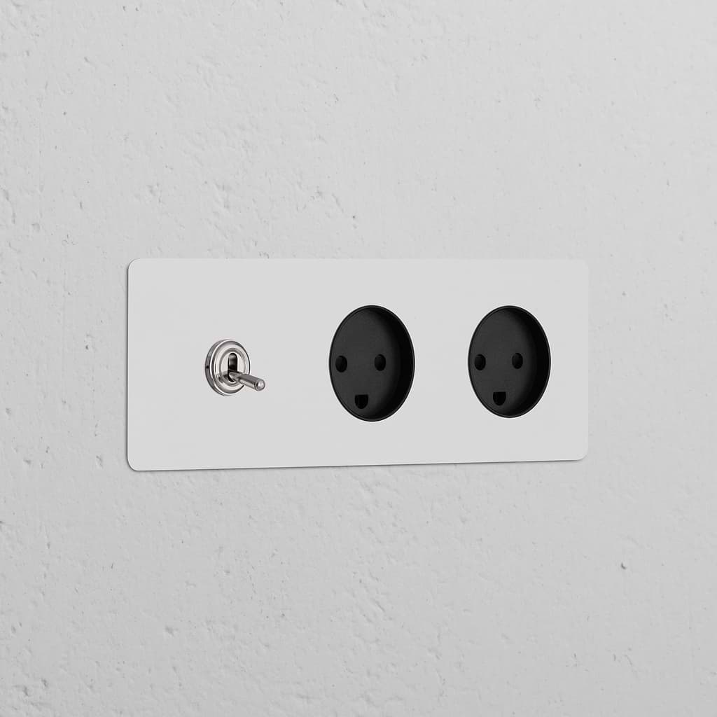 Triple toggle switch and two Danish Type K power modules in paintable polished nickel black on a white wall.