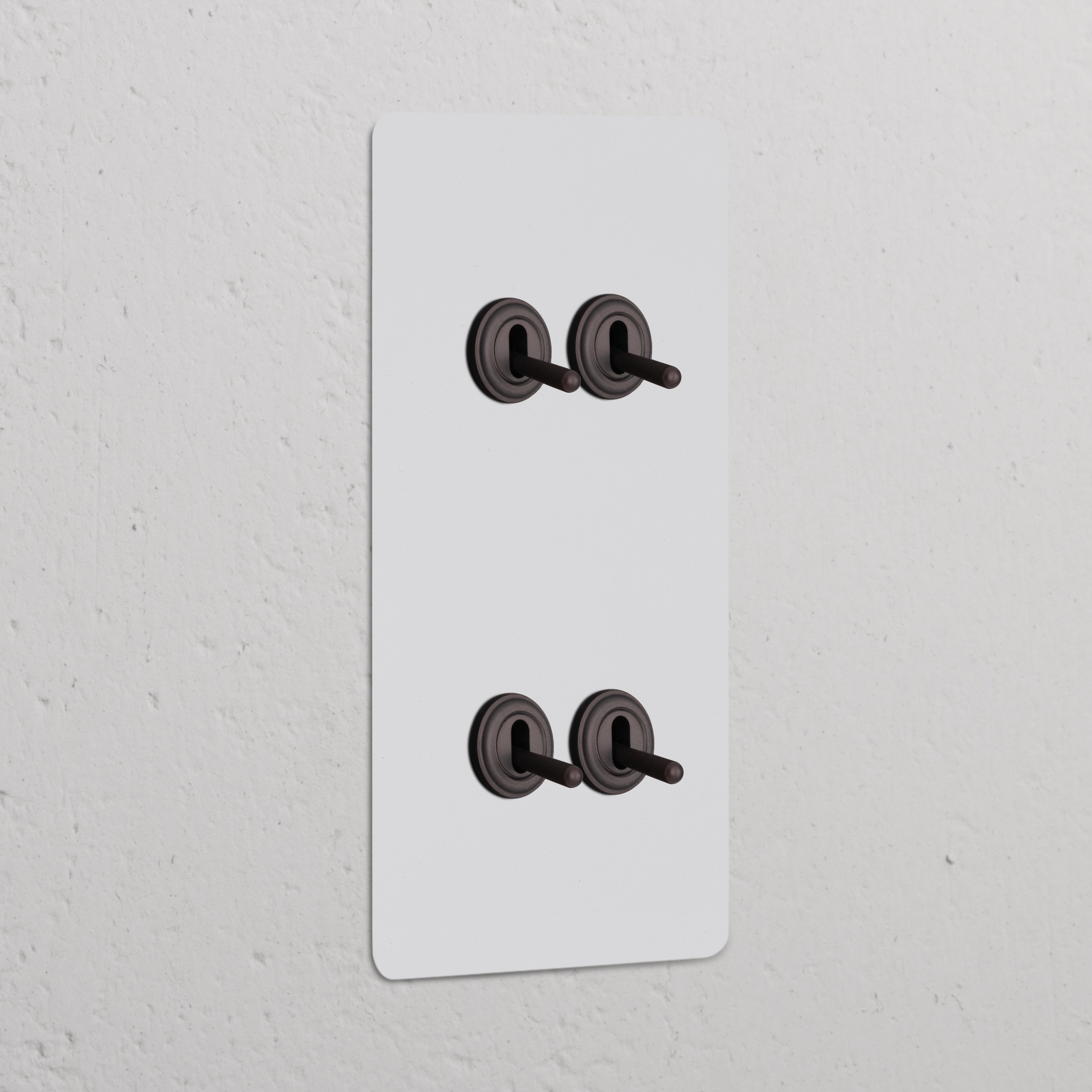 Double 4x vertical toggle switch panel in paintable bronze, featuring sleek design and four toggles on a white wall.