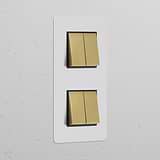 Double 4x Vertical Rocker Switch in antique brass on a black, paintable plate mounted on a textured white wall.