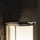 Medium wall light featuring fluted glass shade and polished nickel finish, mounted on a dark textured wall.