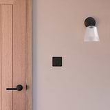 Richmond Medium Wall Light Fluted Glass in Bronze affixed to a wall with a Bronze light switch next to a wooden door with Bronze Apsley door handle