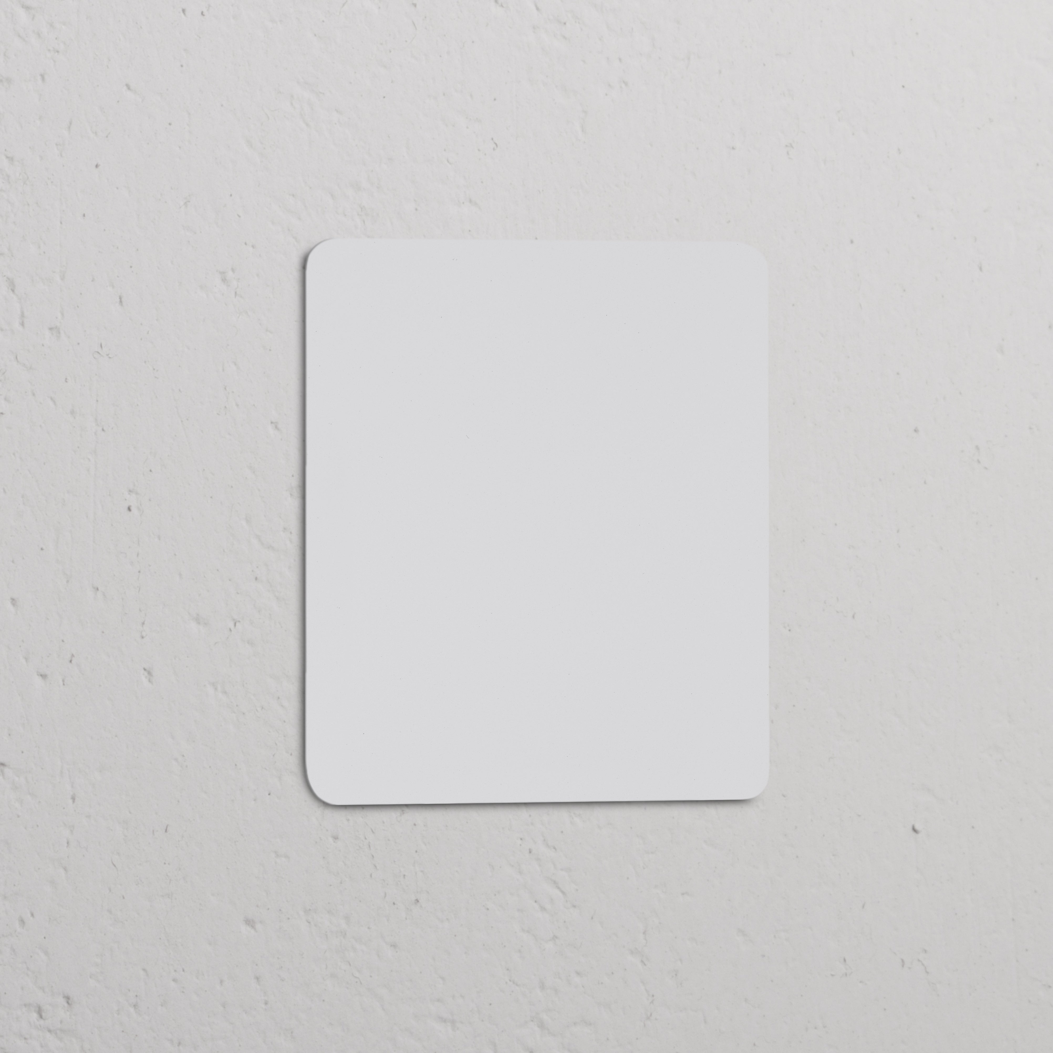 Plaque Obturatrice Simple Peignable blanche pour Prises & Modules Simple, avec coins arrondis sur un mur texturé.