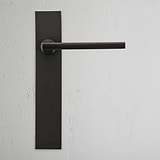 Clayton Poignée de Porte à Ressort à Plaque Longue en bronze montée sur un mur blanc texturé.