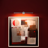 Tableau abstrait aux formes géométriques, éclairé par une lampe à tableau Taylor en nickel poli sur rouge.