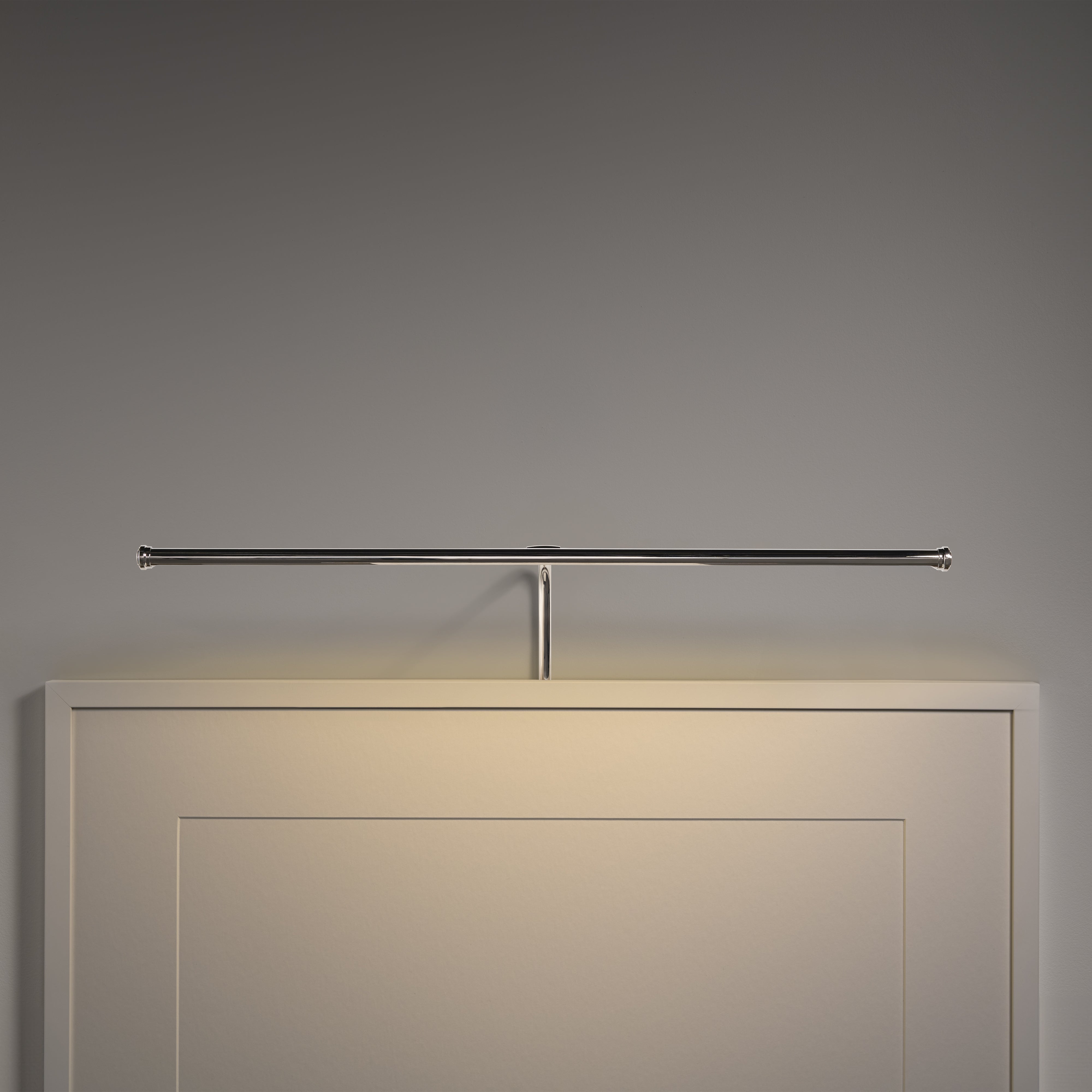 Un élégant luminaire pour tableau Harrow de 580 mm en nickel poli est monté au-dessus d'une œuvre d'art encadrée sur un mur uni.