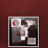 Peinture géométrique dans un cadre blanc sur un mur rouge foncé avec une lumière en bronze au-dessus.