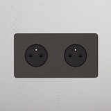 Prise double paroi en bronze Type E x2 avec inserts noirs sur paroi blanche texturée, Prises sur Plaque Double.